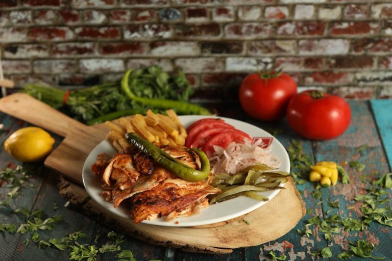 Delicious grilled chicken served with fries, tomatoes, and vegetables on a wooden cutting board.
