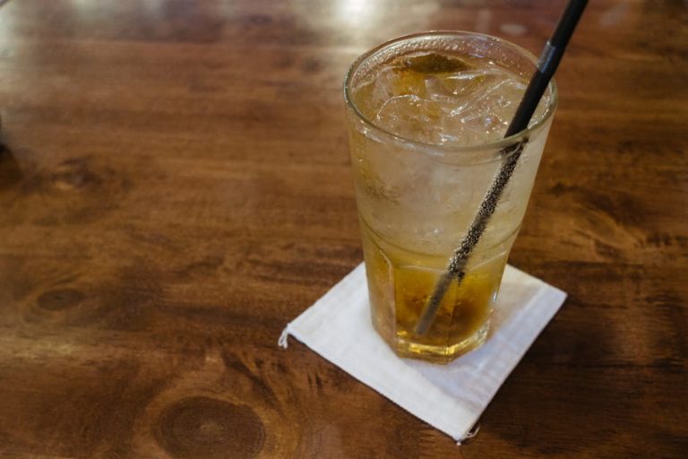 Glass of plum soda with ice cubes on a wooden table, capturing a refreshing moment.