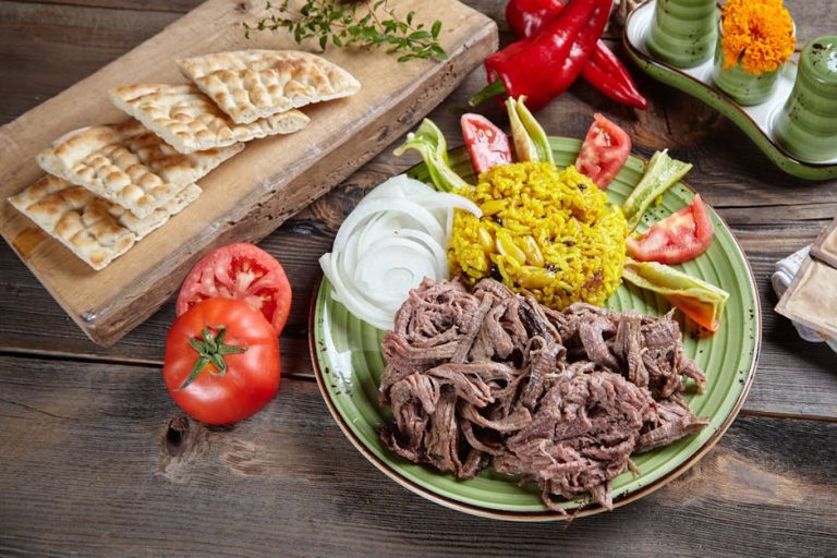 Close-up of a Middle Eastern dish featuring flatbread, spiced rice, vegetables, and shredded meat on a rustic wooden table.
