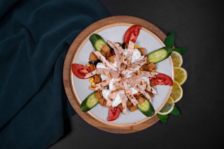 A vibrant grilled chicken salad with fresh tomatoes, cucumbers, and lemon slices on a decorative plate.