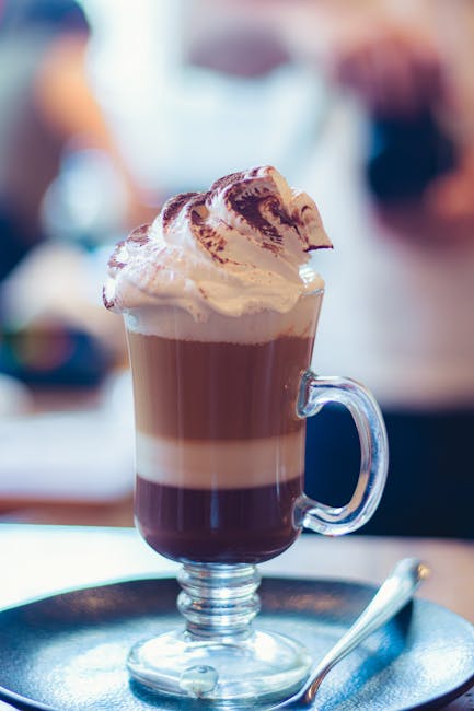 Elegant glass of layered coffee topped with whipped cream and cocoa powder on a plate.