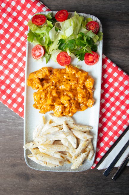 Close-up top view of spicy chicken pasta with fresh salad on a checkered tablecloth.