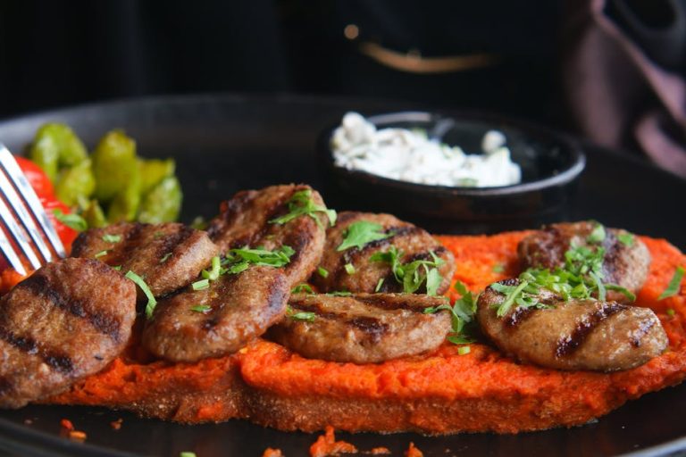 Close-up of grilled meat with red pepper sauce and dipping sauces, garnished with parsley.