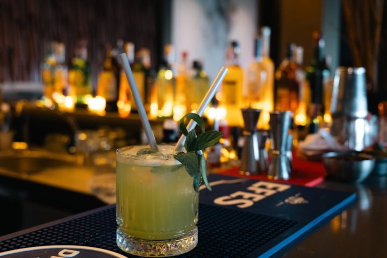 A vibrant, minty cocktail with straws, set against a backdrop of a dimly lit bar.