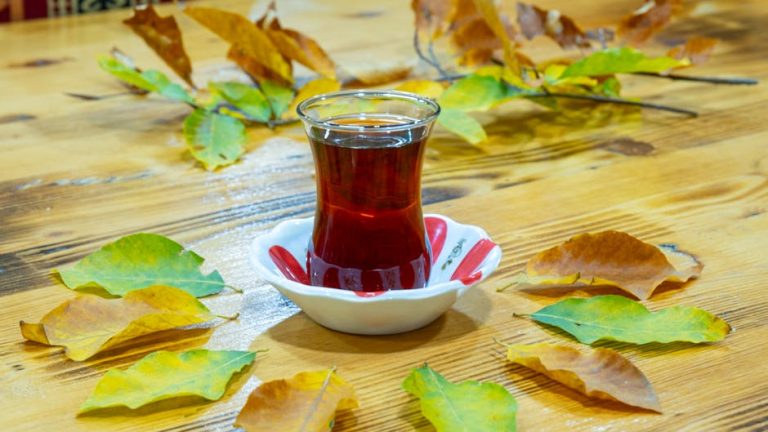 Glass of Turkish tea surrounded by autumn leaves on a wooden table, creating a cozy atmosphere.