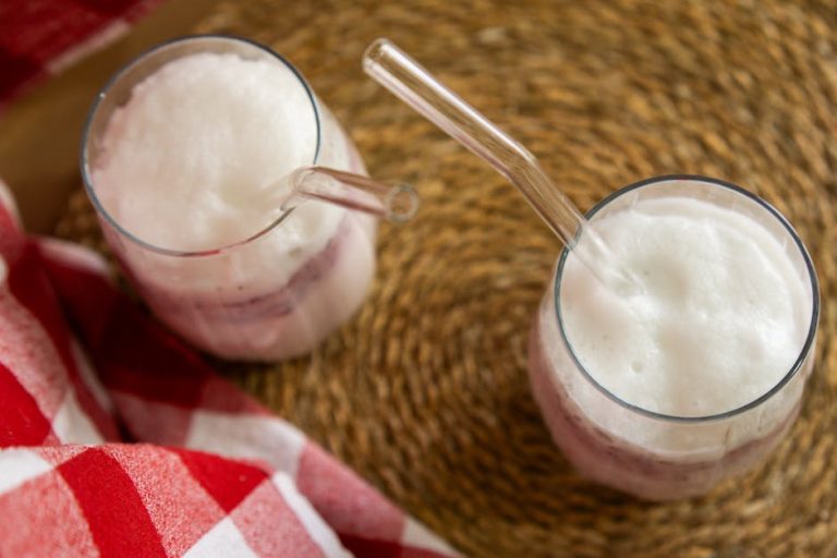 Two foamy iced lattes on a woven placemat with glass straws and red checkered napkin.