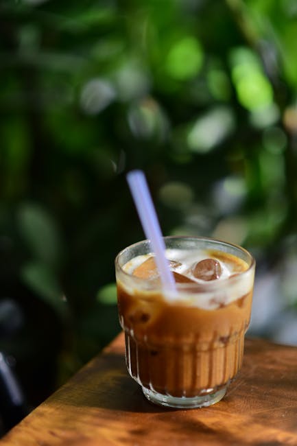 Chilled iced coffee on a wooden table against a lush green background, perfect for refreshing moments.
