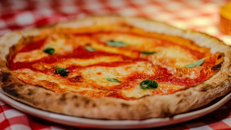 Mouth-watering Margherita pizza with cheese and basil on a classic red checked tablecloth. Perfect food shot.