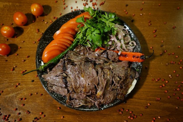 A flavorful grilled meat dish with fresh tomatoes, parsley, and roasted peppers on rustic wooden table.