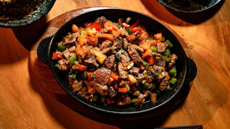 Delicious grilled beef with peppers and tomatoes in a hot skillet on wooden table.