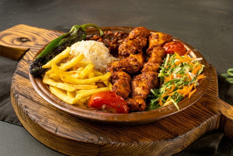 Appetizing grilled chicken with rice, fries, and veggies on a wooden plate.