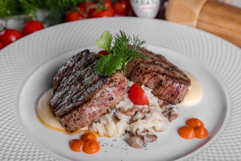 Delicious steak served with mushroom risotto, cherry tomatoes, and herbs on a white plate.