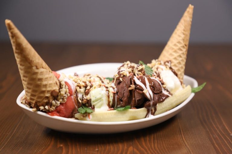Savory banana split topped with ice cream cones and chocolate drizzle in a white bowl.