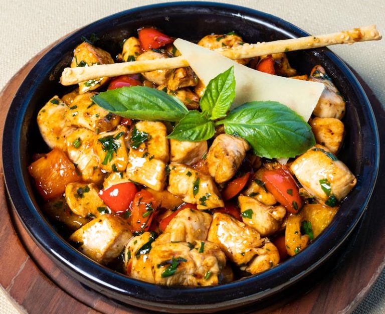 A vibrant grilled chicken salad garnished with fresh basil leaves and served in a rustic bowl.