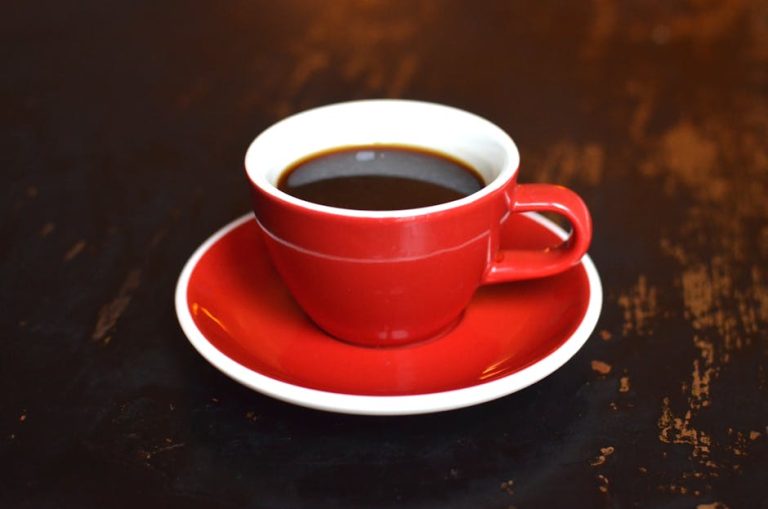 High angle of ceramic cup with aromatic brewed hot coffee placed on wooden table