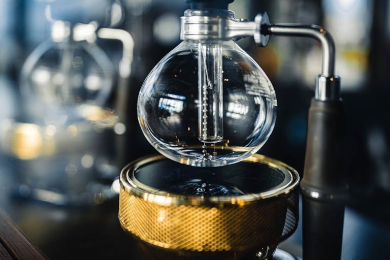 Professional vacuum coffeemaker with glass bottom bowl and burner placed on table in modern coffee house with equipment on blurred background